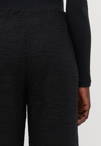 Black textured pants with an elastic waistband. Close-fitting with a soft, woven surface and no visible seams.