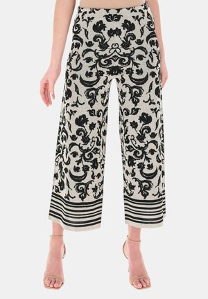 Pantaloni a vita alta a gamba larga con motivo floreale nero su tessuto chiaro, orli a righe orizzontali, abbinati a tacchi color nudo con cinturino alla caviglia.