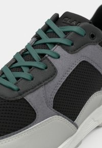 Gray and black sneaker with mesh fabric, textured accents, and teal laces. Features a rubber sole and minimalistic design.