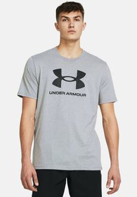 Pelēka kokvilnas t-krekls ar īsām piedurknēm, priekšpusē ar lielu melnu Under Armour logotipu. Arapa dizains, mīksta tekstūra.