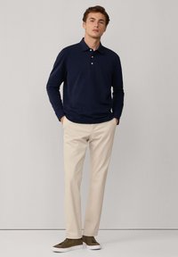 Granatowa koszula polo z długim rękawem z trzema guzikami, w zestawieniu z beżowymi spodniami prostymi i zielono-brązowymi trampkami. Prosty fason i krój.
