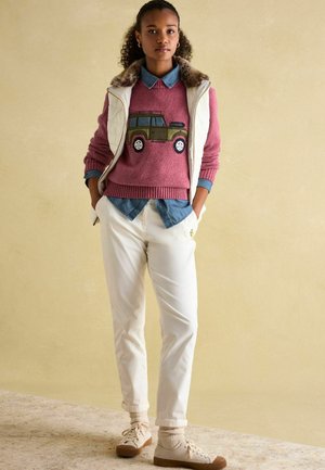 Knitted pink sweater with a green jeep design, layered over a denim shirt. White trousers and beige sneakers complete the outfit.