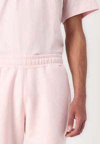 Helles rosa Lounge-Set, bestehend aus einem kurzärmeligen Oberteil und Hose mit elastischem Bund. Weiche Textur mit lockerer Passform und ohne sichtbare Muster oder Akzente.