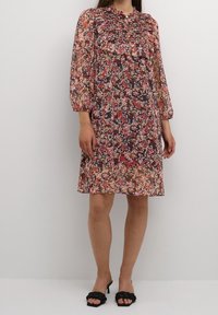Šaty s květinovým potiskem, shromážděným výstřihem, dlouhými rukávy a volným střihem. Vyrobeno z lehké tkaniny v růžových, fialových a oranžových tónech.