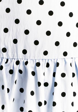 Tela blanca con lunares negros espaciados uniformemente, con un volante fruncido en la parte inferior. Material de algodón texturizado y suave.