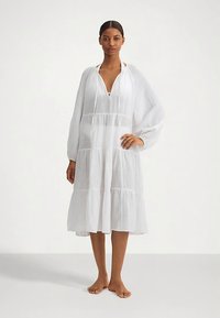 Fehér, réteges ruha könnyű anyagból. Hosszú, felfújt ujjakkal, mély V-nyakkivágással és laza szabással.