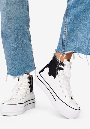 Zapatillas altas blancas con detalles en ante negro, suela de goma plana y puntera texturizada. El diseño incluye secciones de colores contrastantes.