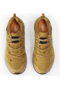 Zapatillas deportivas marrones con material de malla, puntera redondeada y tela texturizada. Presentan cordones elásticos, acentos reflectantes y suelas de goma.