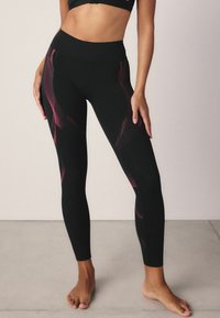 Svarta leggings med hög midja och rosa geometriska prickmönster längs sidorna. Tillverkade av ett stretchigt material för komfort.