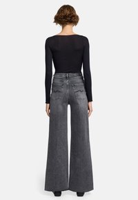 Jean en denim gris à taille haute et jambes larges, avec des poches arrière et une texture douce. Associé à un haut noir ajusté à manches longues.