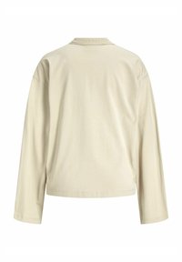 Beige košile s dlouhým rukávem, volného střihu, kulatým výstřihem a měkkou, hladkou texturou. Obsahuje boční rozparky a prošívaný lem.