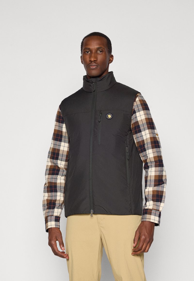Black vest with high collar, zip front, and logo; plaid long sleeves in brown and cream; two front pockets; lightweight fabric.