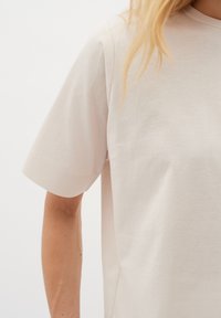 Ljus beige kortärmad t-shirt gjord av mjukt tyg, med en enkel rund halsringning och en slät, otexturerad yta.