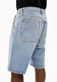 Shorts en denim bleu clair avec poches latérales doubles et deux poches arrière, avec une coupe légèrement ample et un ourlet de longueur standard.