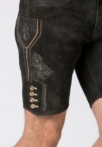 Pantaloni corti in suede marrone scuro con complessi ricami bianchi e bottoni in legno decorativi sul lato. Il design include una tasca con cuciture.