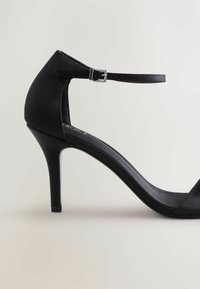 Sort højhælet sandal med en slank satin finish, der har et smalt ankelrem, spids tå og stiletto hæl.