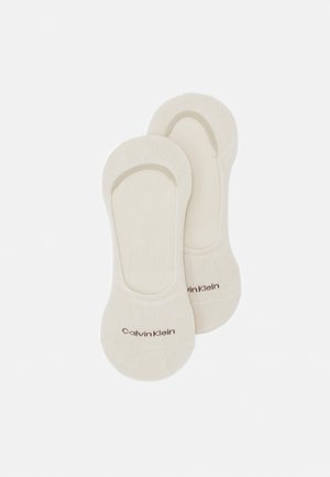 Bež čarape do članka s mekim teksturama, s elastičnim rubovima i printed „Calvin Klein“ logotipom u smeđoj boji. Jednostavan, minimalistički dizajn.