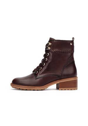 Brown leather ankle boot with lace-up design, gold eyelets, and braided accents. Thick heel and textured rubber sole for grip.