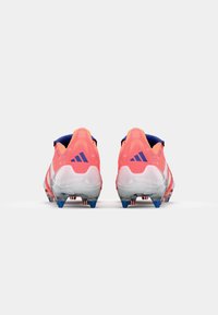 Clavos deportivos Adidas en un vibrante color rosa y blanco, con una superficie texturizada, un acento azul en el talón y una suela con tacos multicolores.
