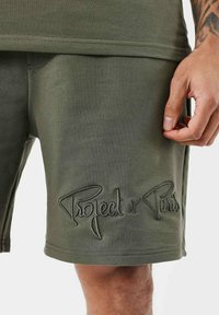 Shorts en coton vert olive avec le logo brodé "Project x Paris", présentant une texture lisse et une coupe décontractée.