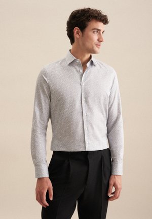 Camicia button-up grigia chiara con piccoli motivi floreali bianchi, maniche lunghe e colletto standard, abbinata a pantaloni neri.