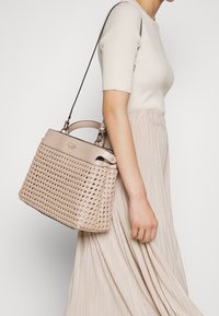 Vævet beige håndtaske med en struktureret design, dobbelt top håndtag og en aftagelig skulderrem, udstyret med et subtilt præget logo.