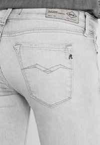 Vaqueros gris claro con un diseño clásico de cinco bolsillos y un distintivo logo bordado en el bolsillo trasero. Textura de denim suave.