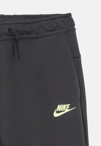 Ciemnoszare dresy Nike z elastycznym paskiem, sznurkiem, bocznymi kieszeniami oraz żółto-zielonym logo Nike na lewym udzie.