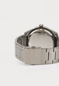 Sølv rustfritt stålarmbåndsur med et polert armbånd, en glatt rund bakke, og en lås med gravert merke.