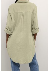 Chemise boutonnée vert clair avec un pli au dos, manches retroussées et ourlet arrondi, confectionnée dans un tissu doux et texturé.