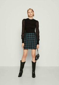 Fekete, hosszú ujjú felső áttetsző csíkos ujjal, kék és fekete kockás mini szoknyával párosítva. A modellen térd fölé érő fekete csizmák vannak.