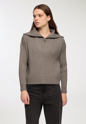 Maglione grigio a coste con colletto con zip, caratterizzato da una finitura texturizzata e una silhouette aderente. Indossato con jeans scuri.