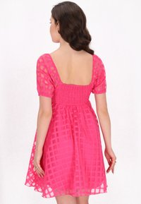 Rosa, halbtransparenter Kleid mit quadratischem Rückenausschnitt, kurzen Puffärmeln und gerüschter Taille. Hat ein karriertes Muster und einen ausgestellten Saum.