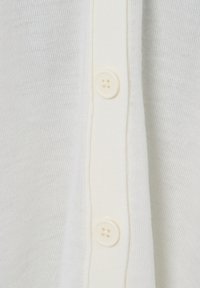 Primo piano di un tessuto lavorato a maglia bianco con due bottoni crema a quattro fori su una pattina verticale.