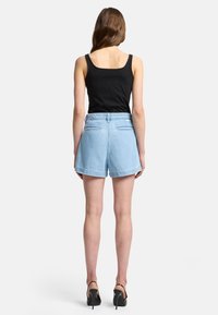 Shorts in denim azzurro chiaro con vestibilità rilassata, orlo risvoltato e due tasche posteriori. Abbinati a un top nero senza maniche e sandali neri con tacco alto.