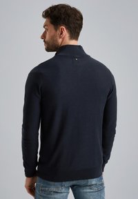 Sweater a collo alto di colore blu navy, realizzato in tessuto a maglia testurizzata, con un piccolo logo sul retro. Rifinito con polsini e orlo a costine.