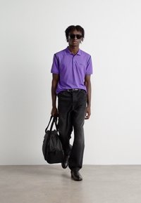 Μωβ πόλο μπλούζα, μαύρα τζιν, γυαλιά ηλίου και μαύρη τσάντα. Στενή γραμμή, κοντά μανίκια, στυλ casual, λεία ύφανση και δερμάτινα παπούτσια.