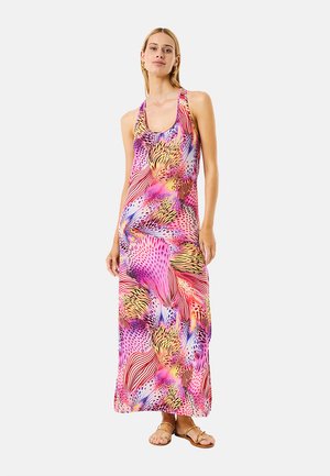 Mujer con un vestido largo sin mangas con estampado abstracto multicolor y sandalias, de pie frente a un fondo liso.