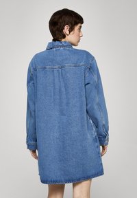 Denimkjole i lyseblå, med krage, lange ermer og løs passform. Har knappede mansjetter og rett fal.