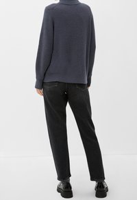 Marineblauer Strickpullover mit hohem Kragen, kombiniert mit lockeren schwarzen Jeans und schwarzen Plateauschuhen. Strukturiertes Gewebe mit gerippten Details.