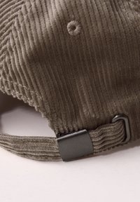 Gorra de pana marrón con textura acanalada, que cuenta con un regulador de metal y un pequeño detalle bordado en la parte superior.