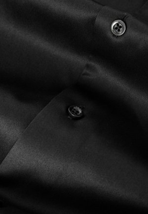 Black fabric shirt with a smooth texture and a subtle sheen. Features a black button with four holes, positioned near the collar.