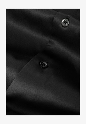 Czarna koszula z tkaniny o gładkiej strukturze i subtelnym połysku. Wyposażona w czarny guzik z czterema otworami, umieszczony w pobliżu kołnierzyka.