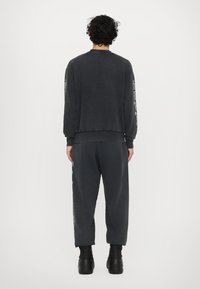 Kulfarvet sweatshirt og matchende joggers i en afslappet pasform med ribbede manchetter. Sorte støvler fuldender outfittet, set fra ryggen.