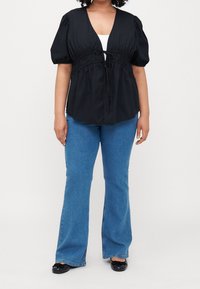 Schwarze Baumwollbluse mit Puffärmeln und verstellbarem Kordelzug in der Taille, kombiniert mit blauen ausgestellt geschnittenen Jeans und schwarzen Ballerinas.