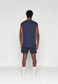 Jūrų mėlynos spalvos be rankovių marškiniai su išlenktu hemu, derinami su juodais šortais. Aprangą užbaigia baltos sportbačiai ir baltos kulkšnių ilgio kojinės.