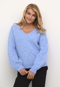 Lichtblauw v-hals sweater gemaakt van pluizig materiaal. Kenmerkt zich door losse, ballonachtige mouwen en geribbelde manchetten. G gedragen met zwarte broek.