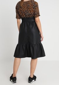 Sort faux lædernederdel med en bølget kant, stylet med en brun mønstret top. Sættet har en tætsiddende talje og afslappede sorte sneakers.