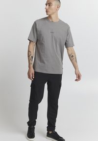 Gray cotton t-shirt with short sleeves, featuring a small logo in the center. Paired with black cargo pants and black sneakers.