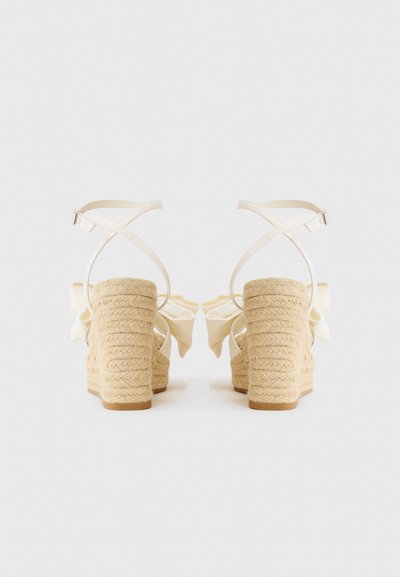 Beige Espadrille-Plateausandalen mit breiten Riemen und einer großen Schleifendetail auf der Rückseite, mit einem strukturierten, gewebten Absatz.